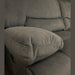 Close-up of the Gibson Electric Recliner, a 3-seater gray upholstered sofa with plush armrests and backrests, set against a dark green wall. The grey washable fabric texture is visible, with a round mirror partly seen at the top right corner.