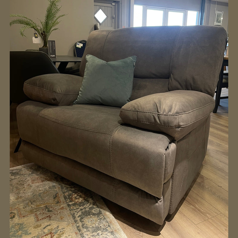 The Gibson Electric Recliner in plush, washable grey fabric with a matching cushion sits on a wooden floor in a modern living room, accompanied by a patterned rug, a small plant table, and filled with natural light.