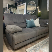 A Gibson Electric Recliner in gray washable fabric with two blue-green and one beige throw pillows rests on a wooden floor in a modern living room featuring green walls, mirrors, and decorative plants.