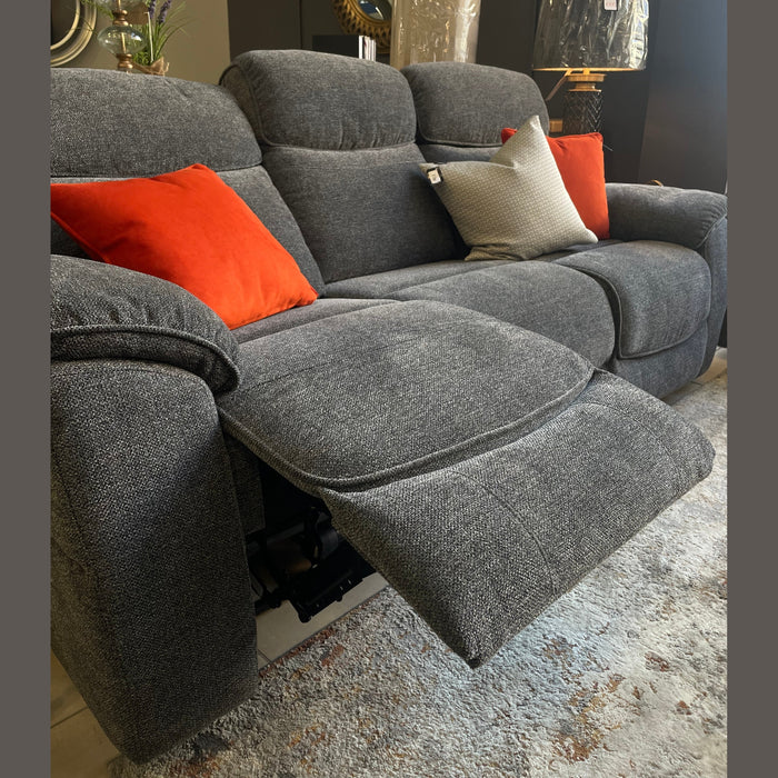 The Asher gray electric reclining sofa with orange and gray cushions is extended in a modern living room, featuring a wireless charging port. Behind it are a patterned rug, lamp, mirror, and decorative items on a side table.