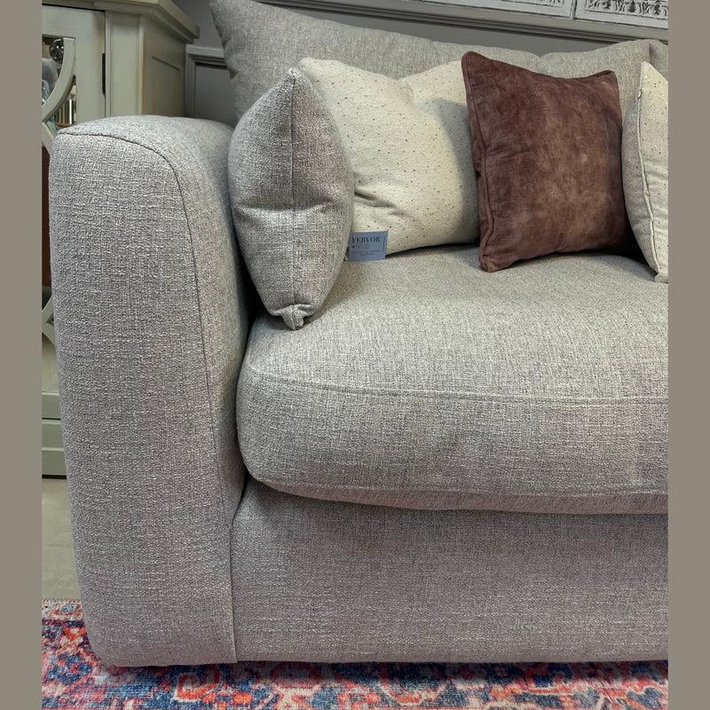 A close-up of the Casablanca Corner Sofa in light gray aqua clean fabric with deep seats, styled with brown and beige cushions on a colorful rug. A £2999 price sign appears in the background alongside ornate wall decor.