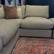 The Casablanca Corner Sofa, featuring deep beige seats and large cushions with a brown accent pillow, sits on a red patterned rug. Circular mirrors decorate the dark blue wall behind it.