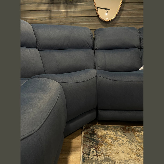 The Dolores Reclining Corner, upholstered in dark blue washable fabric, sits on a wooden floor beside a patterned rug, with a round mirror above reflecting a lamp on the wooden-paneled wall.