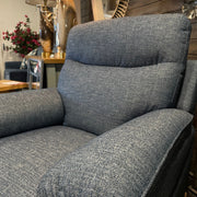 A close-up of the Vera Recliner Sofa in gray fabric highlights its soft, wide armrests and cushioned backrest—ideal for comfy living rooms. In the background, a lamp, plants, and mirror accent the sofa and neutral décor.