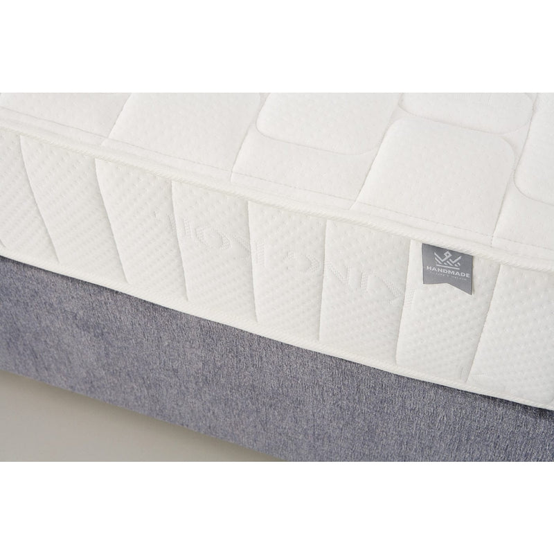 Close-up of a white, quilted King Koil Spinal Guard (ICA) mattress with a textured pattern for posture support on a gray base. A small fabric tag on the mattress reads HANDMADE. Brand: vendor-unknown.