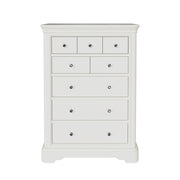 The Mabel Tall Chest by vendor-unknown is a white wooden dresser with seven drawers of various sizes, each with a round silver knob and small curved feet—a chic addition to the Mabel Bedroom Collection.