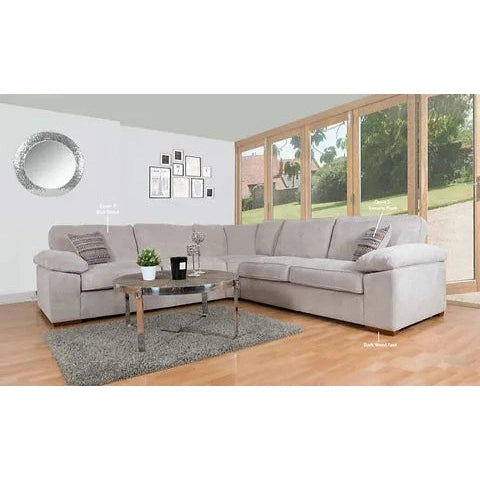 A spacious living room features the Dexter Corner sectional sofa in light gray by vendor-unknown, decorative pillows, a glass coffee table on a gray rug, framed art, a round mirror, and large windows revealing greenery outside.