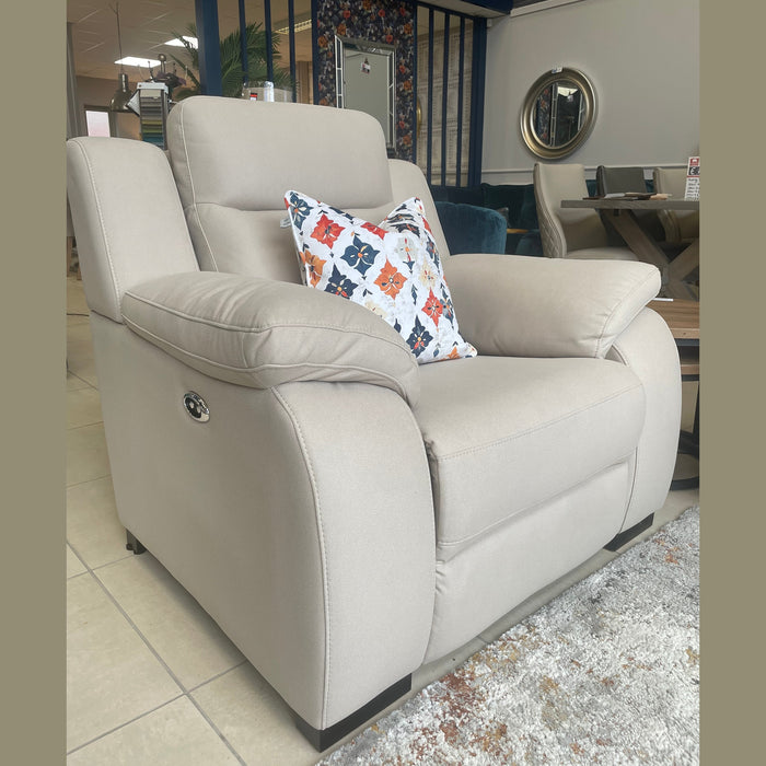 A large modern beige armchair with wide armrests and a colorful geometric pillow is showcased in a showroom, making it the ideal match for your Lorenzo Electric Recliner Sofas.
