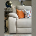 The Lorenzo Electric Recliner Sofa in beige comes with washable fabric, an orange pillow, and a white floral pillow. A round mirror, lamp, and a dining table with flowers are displayed in the background.