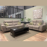 A modern living room setup featuring the Chloe Electric Recliner alongside a contemporary beige sofa, complemented by green patterned cushions, a black coffee table, potted plants, a lamp, and large abstract wall art set against light-colored walls with wood flooring.