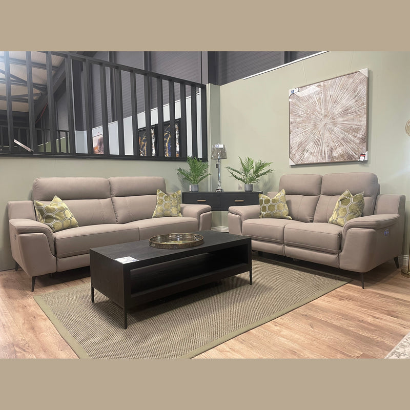 A modern living room setup featuring the Chloe Electric Recliner alongside a contemporary beige sofa, complemented by green patterned cushions, a black coffee table, potted plants, a lamp, and large abstract wall art set against light-colored walls with wood flooring.