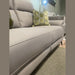 A close-up of the light gray Chloe 3+2 Electric Recliner Sofa with tufted, washable fabric cushions and a hexagonal green pillow. Another sofa and a textured rug are in the background.