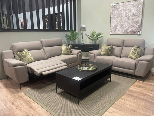 A modern living room with the Chloe 3+2 beige sofas, one featuring an electric recliner, green patterned cushions, a black coffee table, potted plants, a lamp, and abstract wall art on light wood flooring with a beige rug.