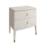 The Diletta Bedside Locker is a modern, light wood nightstand with two drawers, slim metal handles, and slightly tapered legs featuring metallic caps.