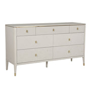 The Diletta Wide 7 Drawer Chest features a modern white finish, gold handles, and gold accents on the legs and corners. Its sleek, minimalist design and spacious drawers make it perfect for stylish bedroom storage.