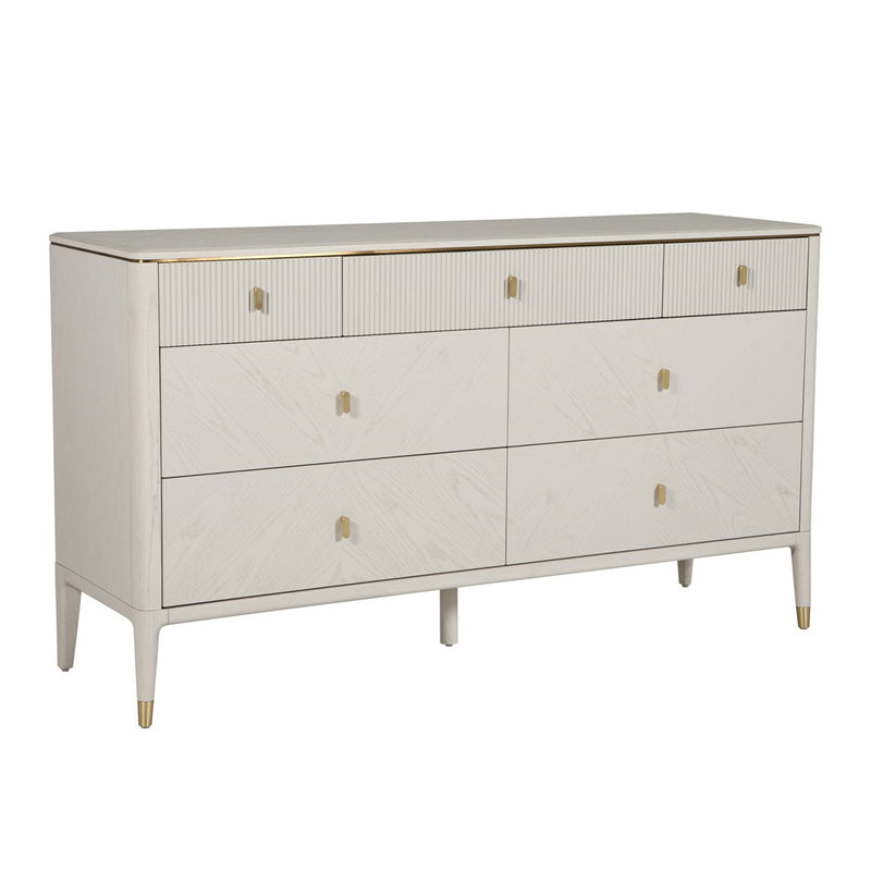 The Diletta Wide 7 Drawer Chest features a modern white finish, gold handles, and gold accents on the legs and corners. Its sleek, minimalist design and spacious drawers make it perfect for stylish bedroom storage.