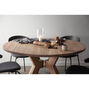 The Monogram Custom Made Table is shown round with four dark chairs, topped with a loaf of bread on a cutting board, a lit glass candle, a mug, small dishes, and draped in a gray cloth against a plain light background.