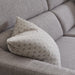 A close-up of the Otis Range light gray fabric sofa with textured upholstery features a patterned cushion by the armrest and another in the background, showcasing its supportive lumbar design for enhanced comfort.
