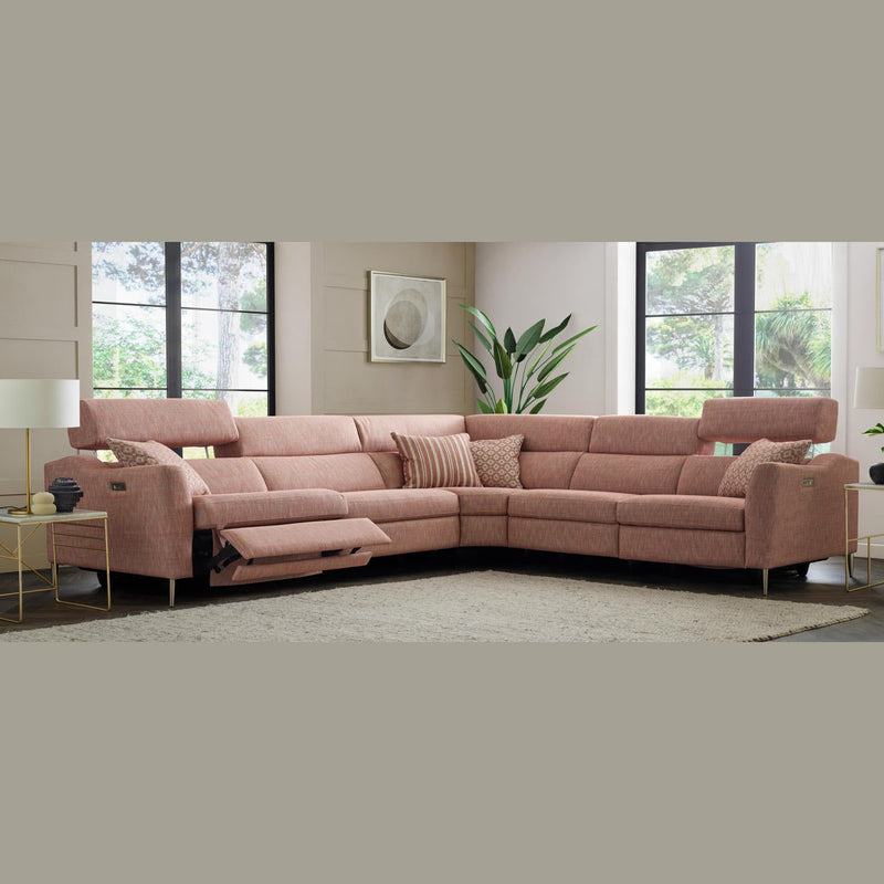 A modern living room with the Otis Sofa Range, a large pink L-shaped sectional in aquaclean fabric, plus adjustable headrests, reclining seats, accent pillows, side tables, a potted plant, wall art, and large windows with outdoor views.