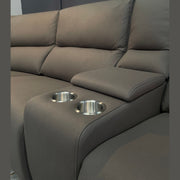 A close-up of the Vegas Corner Group, a modern gray corner sofa with wipeable fabric, stainless steel cup holders in the built-in armrest, set against a dark wall.