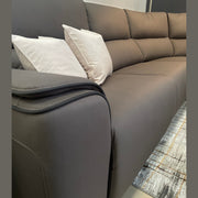 A close-up of the Vegas Corner Group sofa in modern gray, featuring two light beige throw pillows on a patterned rug against a neutral wall with a round mirror above. Its wipeable fabric ensures easy maintenance.