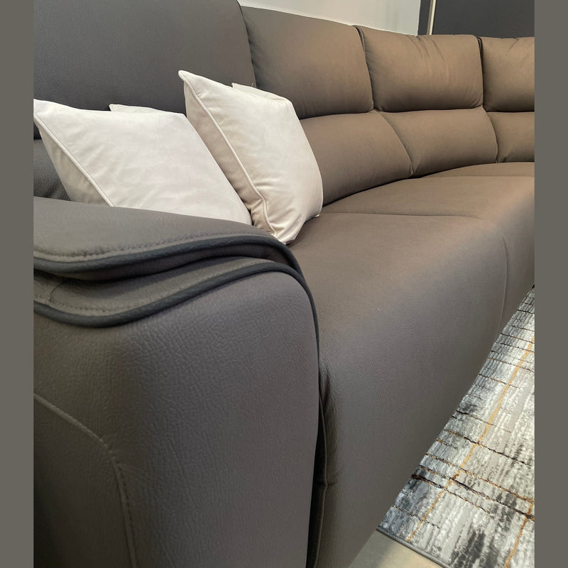 A close-up of the Vegas Corner Group sofa in modern gray, featuring two light beige throw pillows on a patterned rug against a neutral wall with a round mirror above. Its wipeable fabric ensures easy maintenance.
