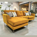 The Turino Chaise, a modern mustard yellow sectional made in Ireland with durable Aquaclean fabric, is showcased in a bright living space featuring large windows, potted plants, and minimalist decor.