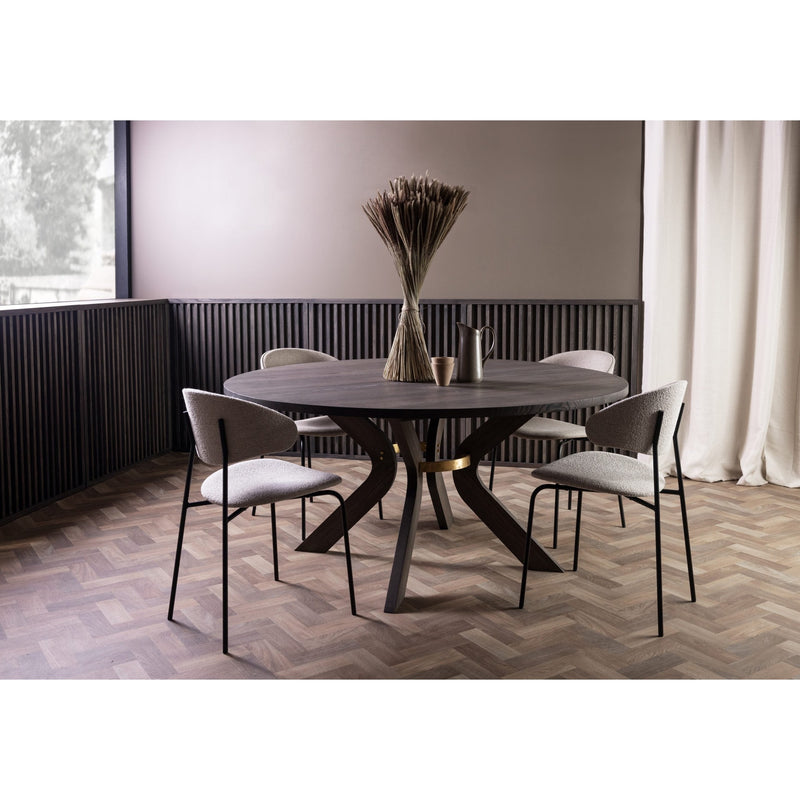 A modern round dining table made of ash wood, with a central decorative vase on the table, surrounded by four chairs with upholstered seats. The table is placed in a room with parquet flooring and a large window.