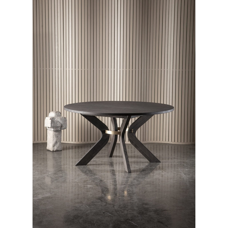 The Sydney Round Dining Table with angled legs stands on a polished concrete floor before vertical beige slats, with a small abstract stone sculpture placed to its left.