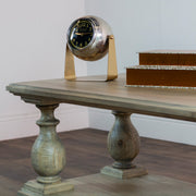 The Marwood Coffee Table with ornate legs (120 cm wide, 45 cm high) holds a vintage-style clock with gold accents. Two decorative brown boxes are stacked nearby, all set against a plain white wall.