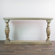 The Marwood Large Console Table, featuring a rectangular wood top, ornate carved legs, and a matching bottom shelf (82 cm high, 150 cm wide), is placed against a white wall on a wooden floor.