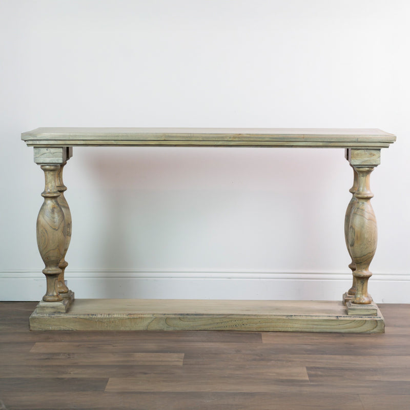 The Marwood Large Console Table, featuring a rectangular wood top, ornate carved legs, and a matching bottom shelf (82 cm high, 150 cm wide), is placed against a white wall on a wooden floor.