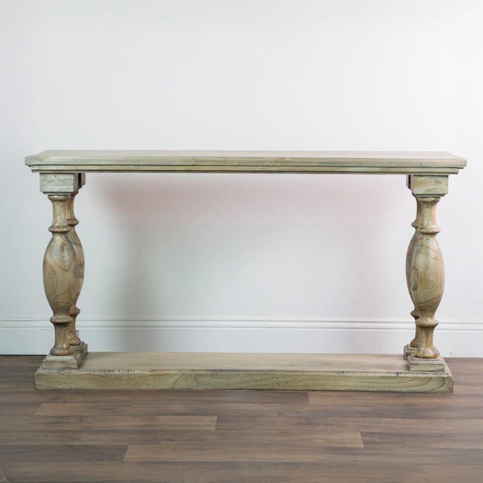 The Marwood Large Console Table, featuring a rectangular wood top, ornate carved legs, and a matching bottom shelf (82 cm high, 150 cm wide), is placed against a white wall on a wooden floor.