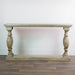The Marwood Large Console Table, featuring a rectangular wood top, ornate carved legs, and a matching bottom shelf (82 cm high, 150 cm wide), is placed against a white wall on a wooden floor.