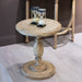 The Marwood Round Side Table (50 cm wide, 57 cm high) with a pedestal base stands on a light wood floor, displaying two black-framed hourglasses. A wooden chair is partially visible in the background.