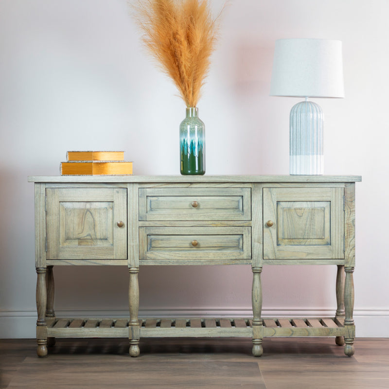 The Marwood Large Sideboard Console (150 cm wide, 82 cm high) features two cabinets and two drawers, topped with a green vase of pampas grass, a white lamp, and yellow boxes, set against a light wall on wooden flooring.