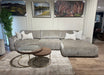 A modern living room featuring the Opus Chaise, a large gray contemporary sectional, four decorative pillows, a nested round glass and wood coffee table, beige rug, wall art, and wood flooring.