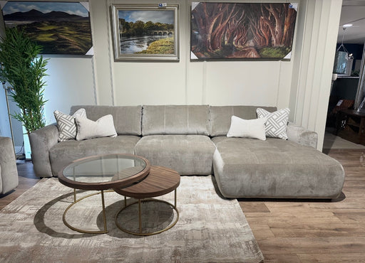 A modern living room featuring the Opus Chaise, a large gray contemporary sectional, four decorative pillows, a nested round glass and wood coffee table, beige rug, wall art, and wood flooring.