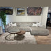 A modern living room featuring the Opus Chaise, a large gray contemporary sectional, four decorative pillows, a nested round glass and wood coffee table, beige rug, wall art, and wood flooring.