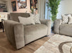 A modern living room featuring two Opus Swivel Cuddlers in plush gray Aquaclean fabric, decorative pillows, a beige patterned rug, potted green plant, and framed artwork. Wooden floors and natural light complete the contemporary look.