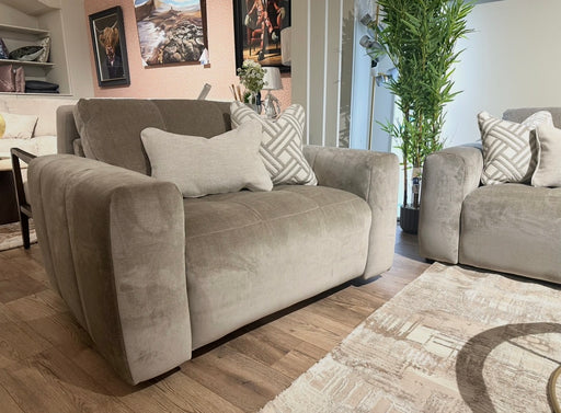 A modern living room featuring two Opus Swivel Cuddlers in plush gray Aquaclean fabric, decorative pillows, a beige patterned rug, potted green plant, and framed artwork. Wooden floors and natural light complete the contemporary look.