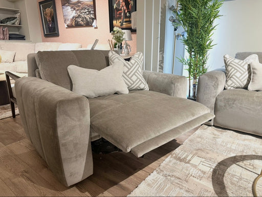The Opus Swivel Cuddler, a gray upholstered recliner with extended footrest, anchors a modern living room featuring matching armchairs, patterned pillows, wall art, a tall plant, and light wood flooring.