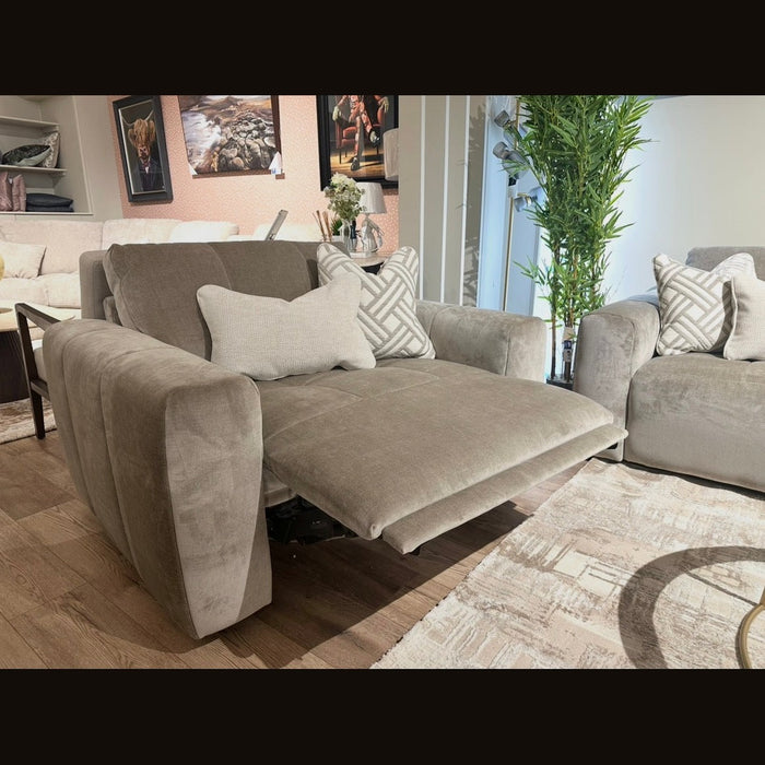 The Opus Swivel Cuddler, a gray upholstered recliner with extended footrest, anchors a modern living room featuring matching armchairs, patterned pillows, wall art, a tall plant, and light wood flooring.