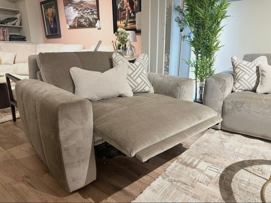 The Opus Swivel Cuddler, a gray upholstered recliner with extended footrest, anchors a modern living room featuring matching armchairs, patterned pillows, wall art, a tall plant, and light wood flooring.