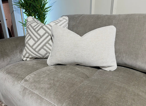 The Opus Chaise is a gray upholstered, contemporary modular sofa featuring two decorative pillows—one geometric and one textured beige—and pairs beautifully with greenery for a fresh, modern vibe.