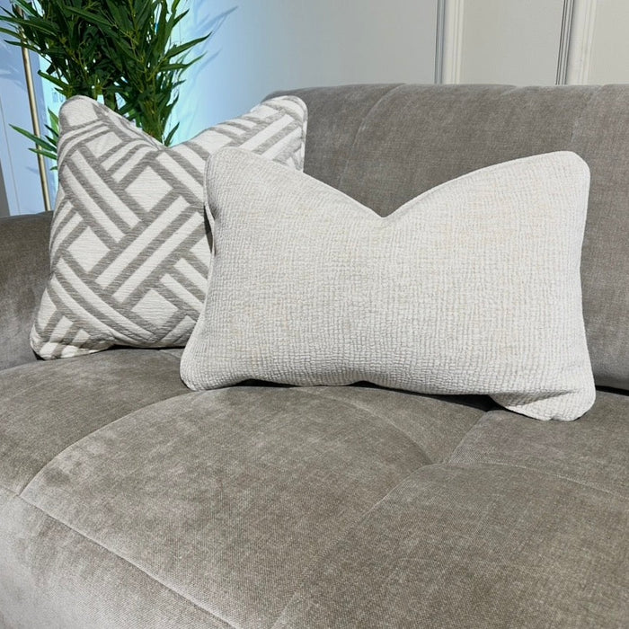 The Opus Chaise is a gray upholstered, contemporary modular sofa featuring two decorative pillows—one geometric and one textured beige—and pairs beautifully with greenery for a fresh, modern vibe.