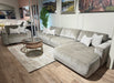 A modern living room featuring the Opus Chaise in a light gray modular design, matching armchair, Aquaclean Fabrics pillows, round wooden coffee table, beige rug, indoor plant, and landscape paintings on the wall.
