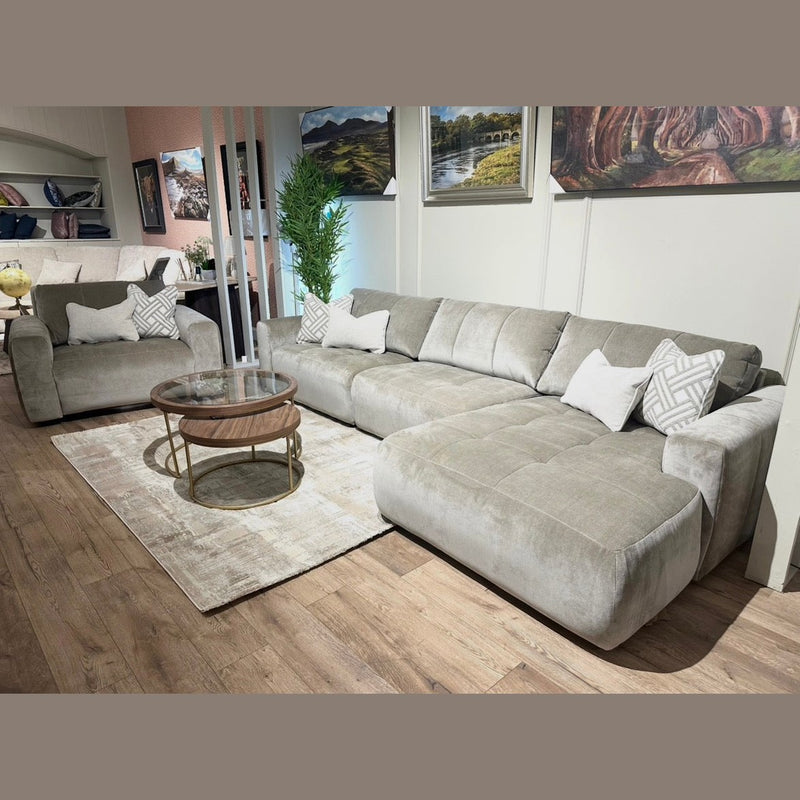 A modern living room with the Opus Swivel Cuddler in light gray, matching armchair, white and patterned pillows, a round wooden coffee table, beige rug, and landscape paintings on the wall.