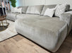 The Opus Chaise is a spacious, light gray sectional sofa with plush cushions in Aquaclean Fabrics, featuring a contemporary design and accented with patterned and solid throw pillows. It’s paired with a round coffee table on a beige rug.