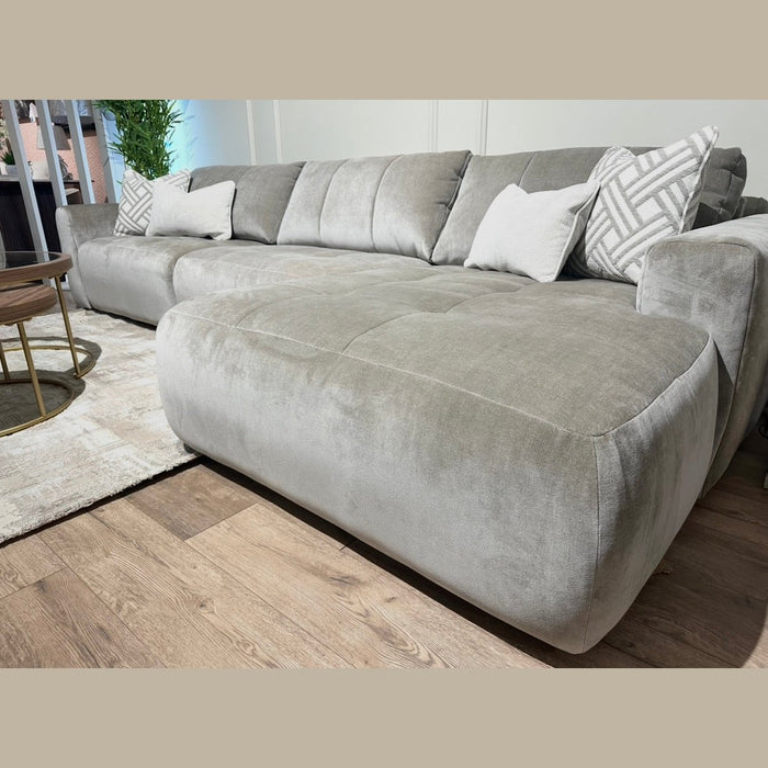 The Opus Chaise is a spacious, light gray sectional sofa with plush cushions in Aquaclean Fabrics, featuring a contemporary design and accented with patterned and solid throw pillows. It’s paired with a round coffee table on a beige rug.